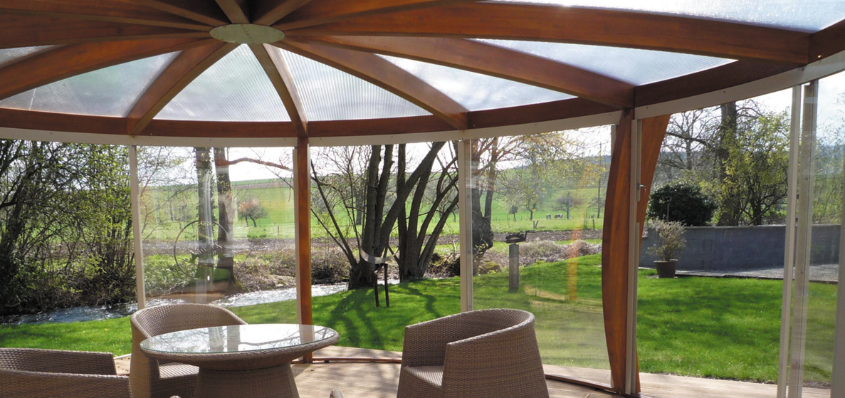 Véranda d'une maison, avec un toît en polycarbonate alvéolaire translucide, donnant vue sur un jardin